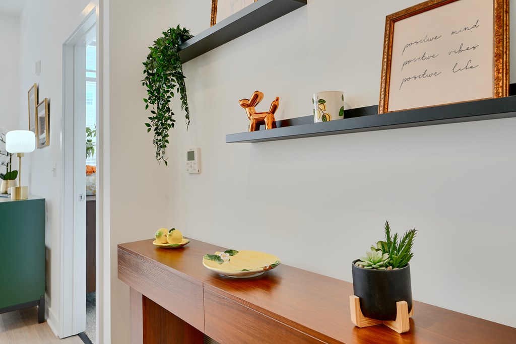 Now leasing senior 1-bedrooms in Baltimore, MD. A wooden table with a plant and a framed picture on it.