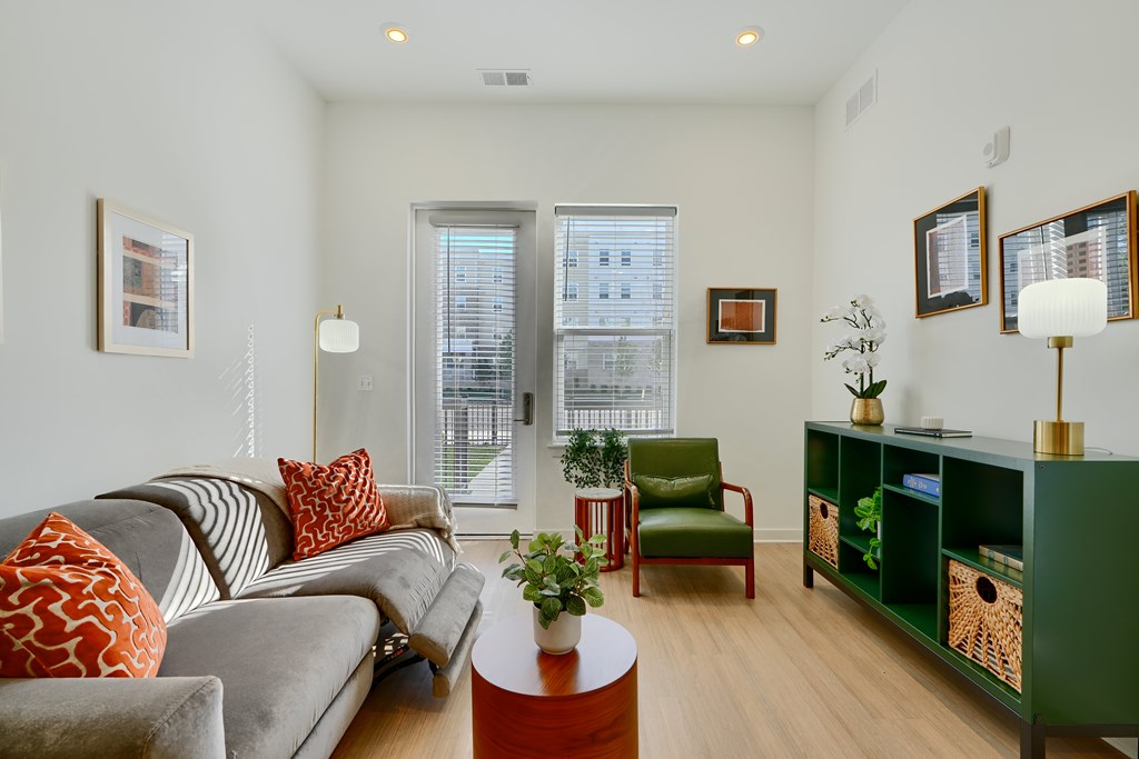 Now leasing senior 1-bedrooms in Baltimore, MD. A living room with a grey couch, a green chair, and a green bookshelf.