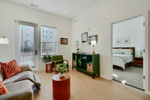 Now leasing senior 1-bedrooms in Baltimore, MD. A living room with a grey couch and a red pillow.