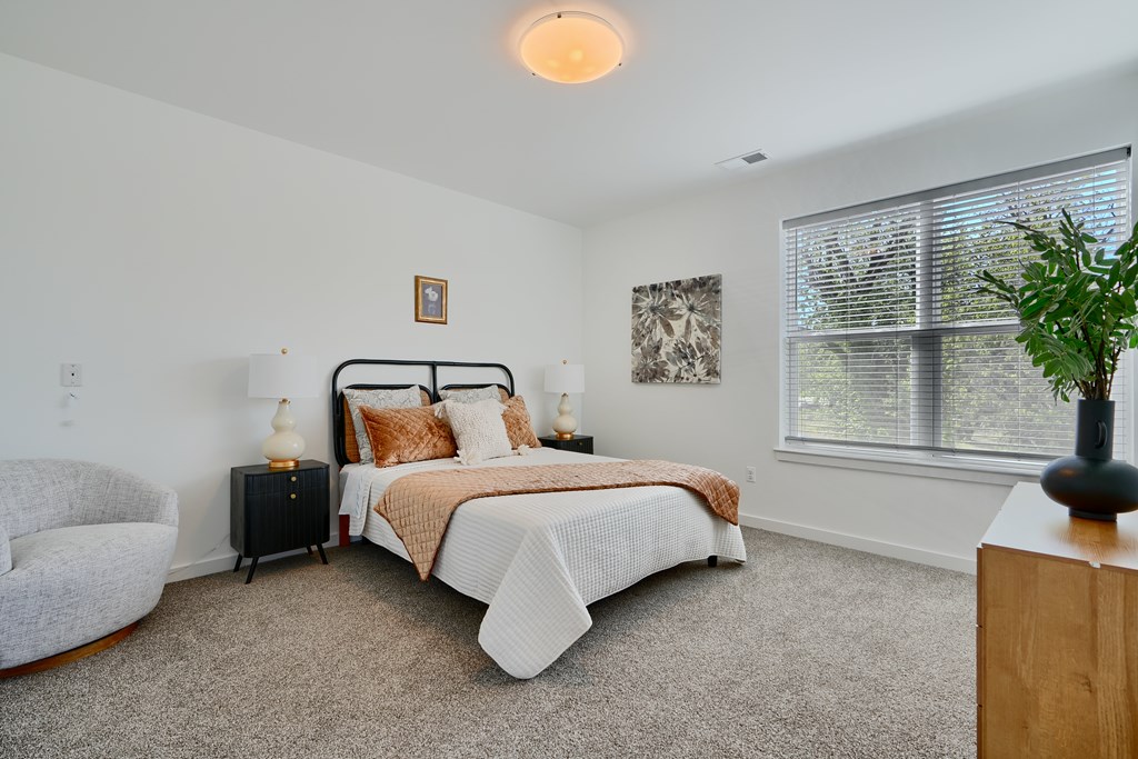 Now leasing senior 1-bedrooms in Baltimore, MD. A bedroom with a bed, chair, and window.