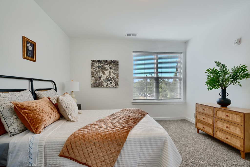 Now leasing senior 1-bedrooms in Baltimore, MD. A bedroom with a bed, dresser, and window.