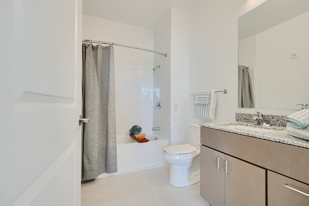 Now leasing senior 1-bedrooms in Baltimore, MD. A white toilet sits in a bathroom with a white shower curtain.