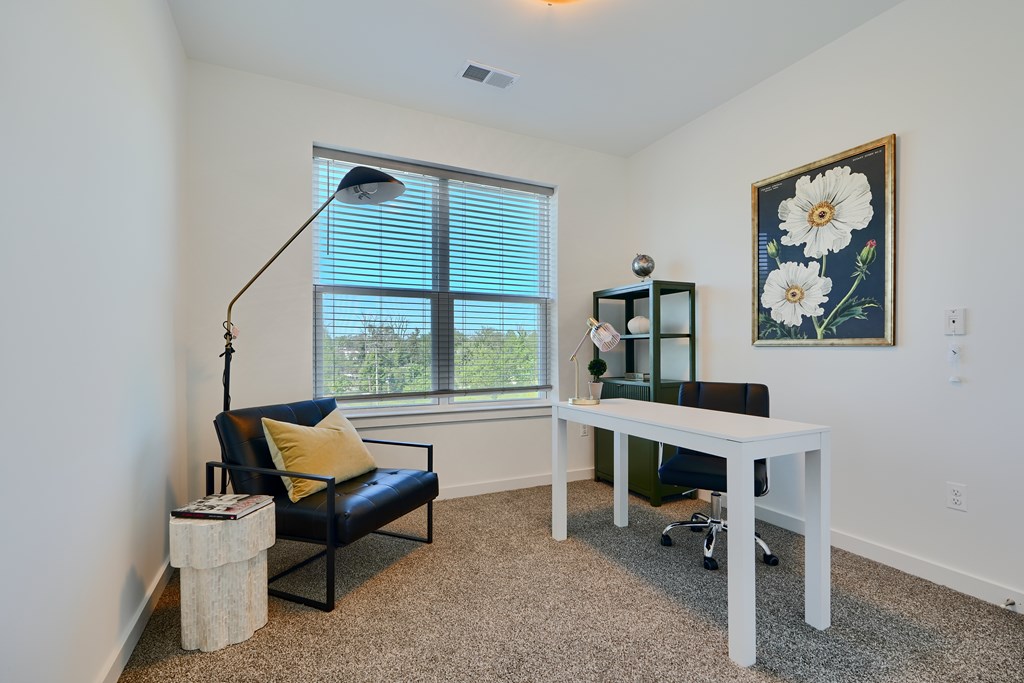 Now leasing senior 1-bedrooms in Baltimore, MD. A room with a black chair, a white desk, and a painting of flowers on the wall.