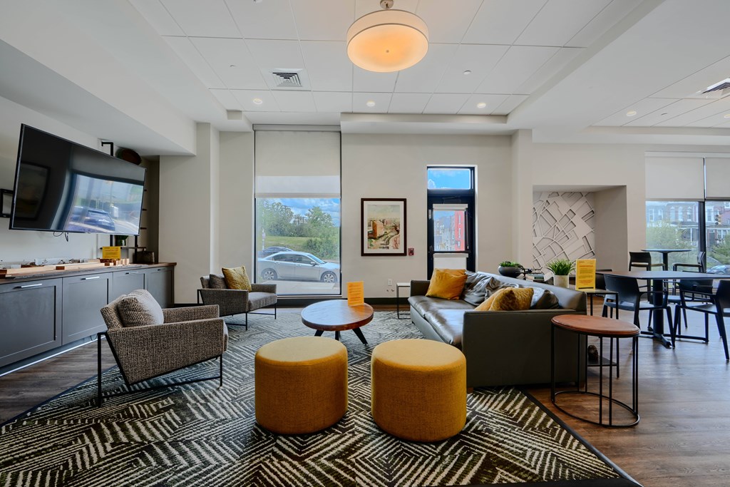 A living room with a grey couch, a yellow ottoman, and a television.