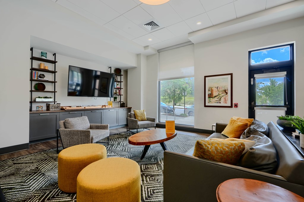 A living room with a grey couch, yellow ottoman, and a television.