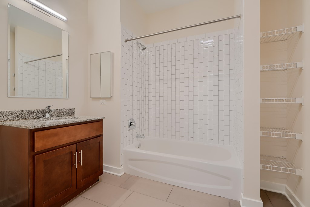 A white tiled bathroom with a wooden vanity and a walk-in shower.