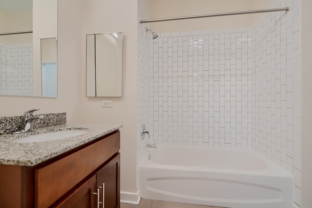 A white tiled bathroom with a wooden vanity and a white bathtub.