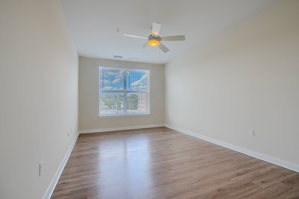 A room with a ceiling fan and a window showing a view of a city.