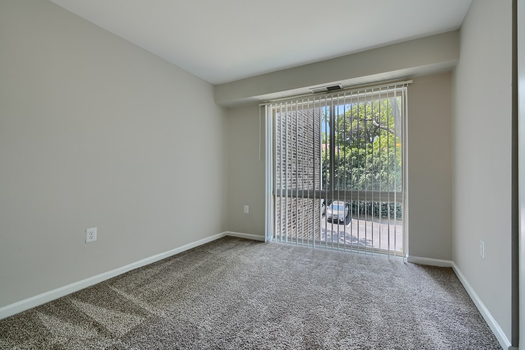 A room with a carpeted floor and a sliding glass door leading to a balcony.