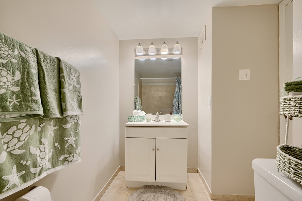 A white cabinet with a mirror above it is in a bathroom.