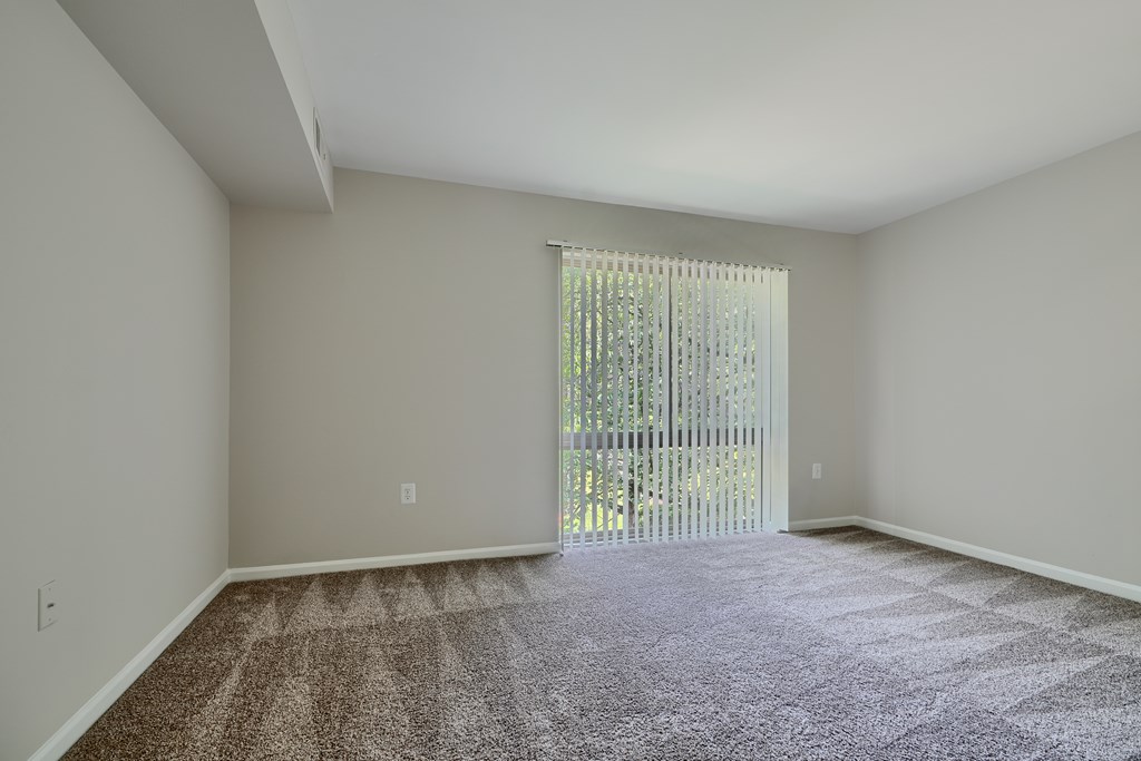 A room with a carpeted floor and a sliding glass door leading to a balcony.