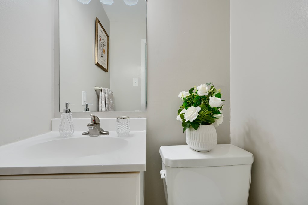 A white toilet sits next to a sink with a vase of flowers on top.