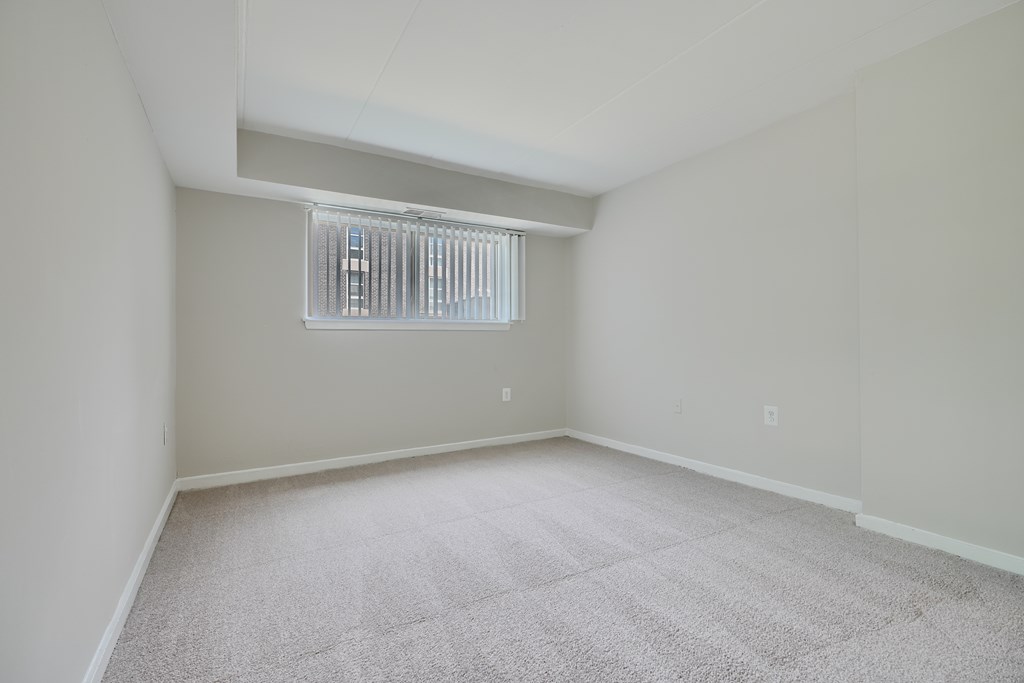 A room with a carpeted floor and a window with blinds.