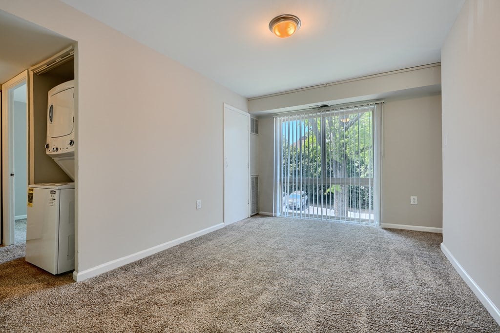 A spacious room with a carpeted floor and a window with blinds.