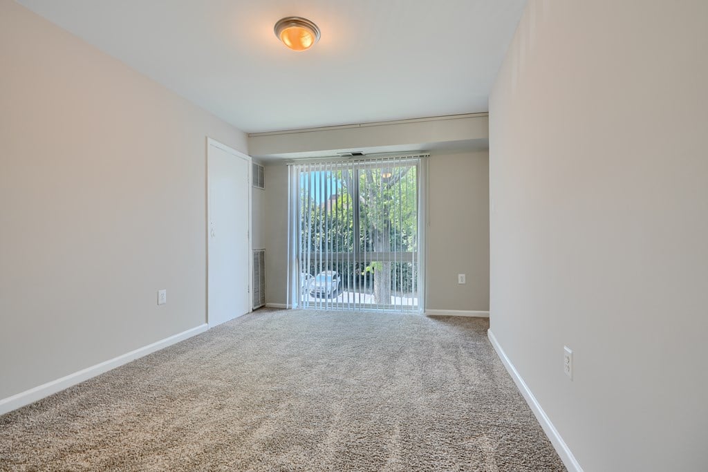 A room with a carpeted floor and a sliding glass door leading to a balcony.