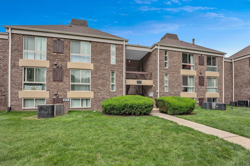 a brick apartment building with green grass and a sidewalk