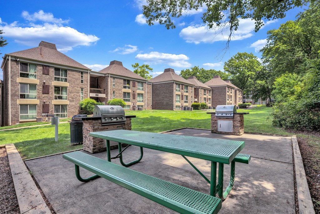 a green picnic table in front of an apartment building with barbecue pits