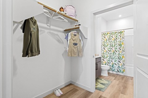 a bathroom with a shower and a closet with clothes hanging on the wall