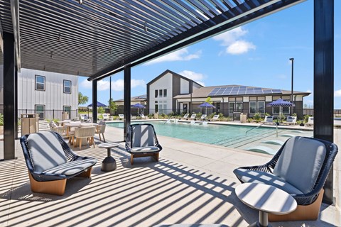 Pool at The Esther apartments in Converse, TX with tanning deck, lounge seating and umbrellas.