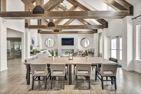 Spacious common area with a combination of lounge seating and a long dining table, highlighted by exposed wood beams, natural light, and modern amenities.