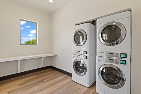 Two front load washing machines in a laundry room with a window showing the sky.