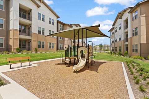 A playground area with a slide and swing set in front of apartment buildings.