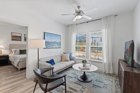 A living room with a white couch, a chair, a bed, a ceiling fan, and a painting on the wall.