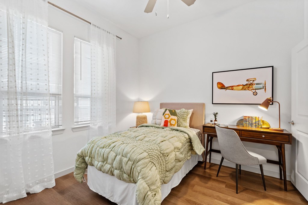 A bedroom with a bed, desk, chair, and a picture of a vintage airplane on the wall.