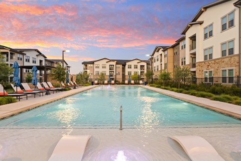 A large outdoor pool surrounded by lounge chairs and buildings.