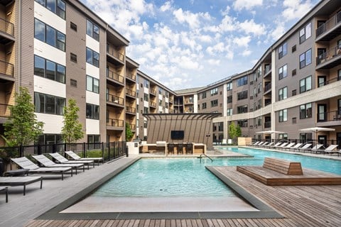 A large outdoor pool surrounded by lounge chairs and apartment buildings.