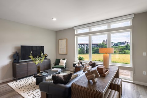 A living room with a black couch, a wooden coffee table, and a large window with a view of the outdoors.