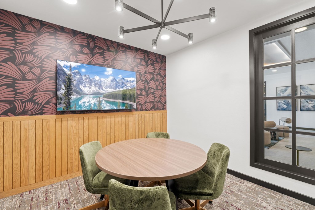 A conference room with a large screen on the wall and a table with chairs.