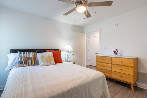 Light-filled bedroom with a cozy bed, soft accent pillows, and dresser storage, designed for everyday comfort and relaxation.