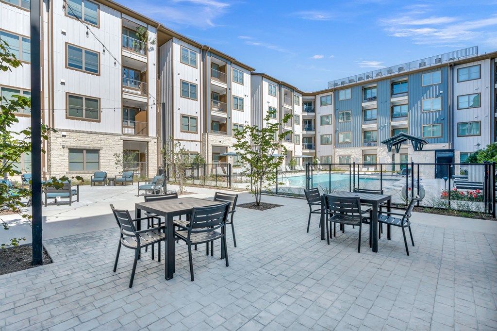 a patio with tables and chairs in front of an apartment building