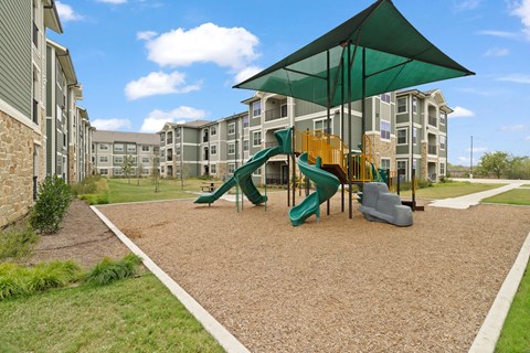 Community playground featuring colorful slides, climbing structures, and a shaded play area surrounded by modern apartment homes.
