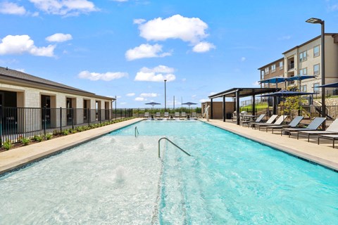 Community pool featuring a tanning ledge, lounge seating, and shaded relaxation areas.