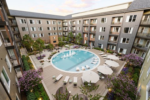 A pool surrounded by loungers and umbrellas in a courtyard surrounded by apartment buildings.