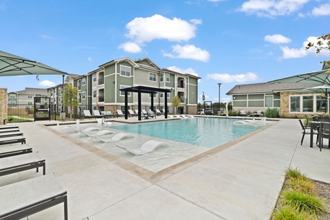 Resort-style swimming pool featuring a spacious sun deck, comfortable lounge seating, and modern apartment homes in the background.