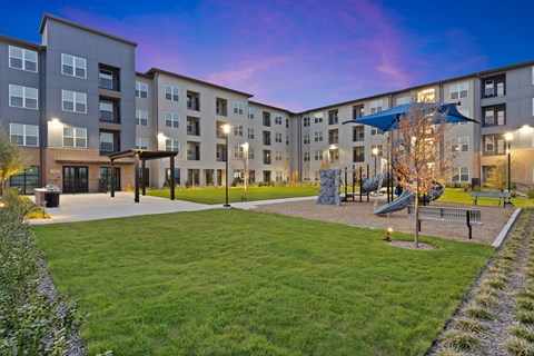 Landscaped courtyard with open green space, shaded playground, and modern apartment buildings surrounding a central lawn.