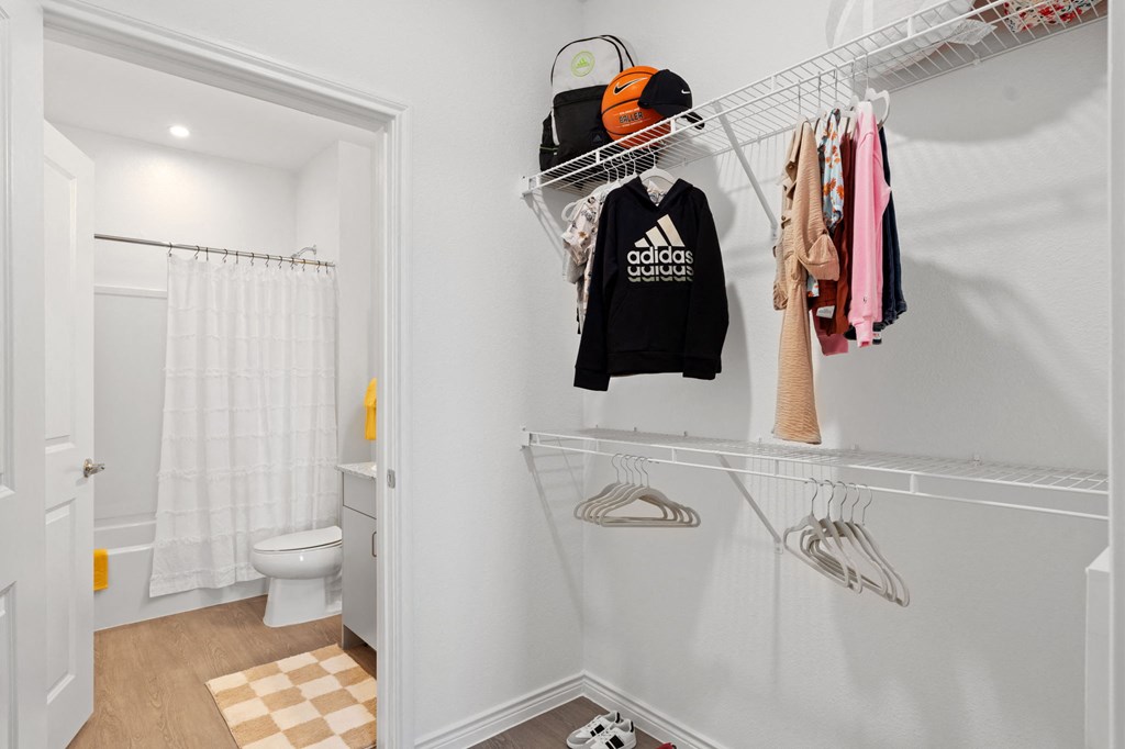 a bathroom with a shower and a closet with clothes hanging on a rack in it