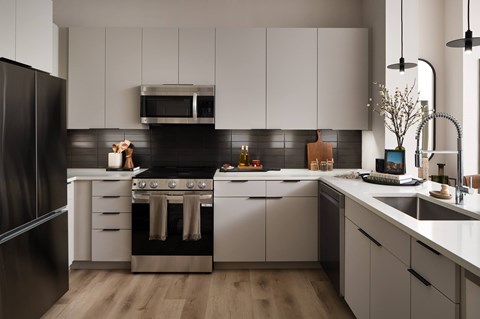 A modern kitchen with a black refrigerator, stainless steel oven, and white cabinets.