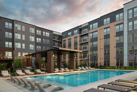 A modern apartment complex with a pool and lounge chairs.