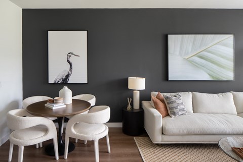A living room with a white couch, a round table with four chairs, and two framed pictures on the wall.