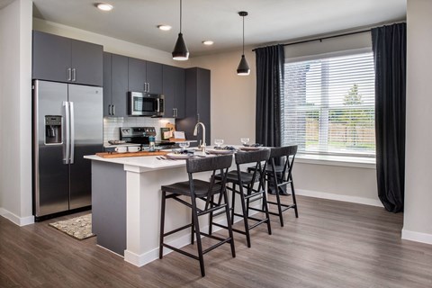 A kitchen with a refrigerator, microwave, and a dining table with chairs.