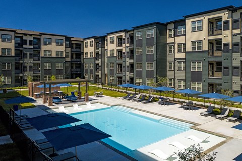 A swimming pool surrounded by apartment buildings and lounge chairs.
