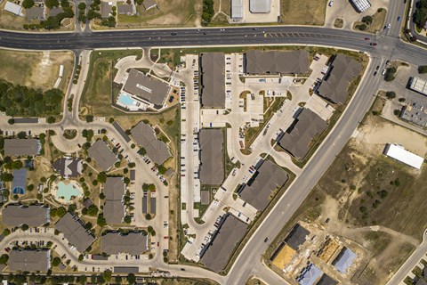 Overhead view of a large apartment property with rows of buildings, structured parking lots, and shared outdoor spaces connected by sidewalks