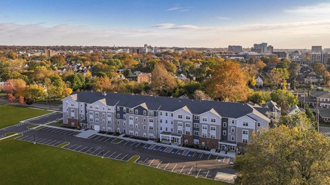 Aerial view of a modern apartment building surrounded by mature trees, open green space, and a vibrant neighborhood setting.