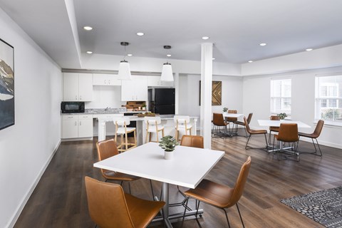 Open resident lounge featuring dining tables, comfortable seating, and a kitchen area with a breakfast bar and stools.