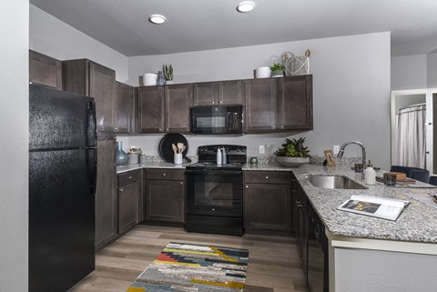 A kitchen with a black refrigerator and brown cabinets.