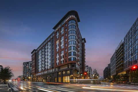 A street view of Emblem Apartments in the NOMA neighborhood of DC A long exposure shot of a city street at dusk with a modern building in the foreground.